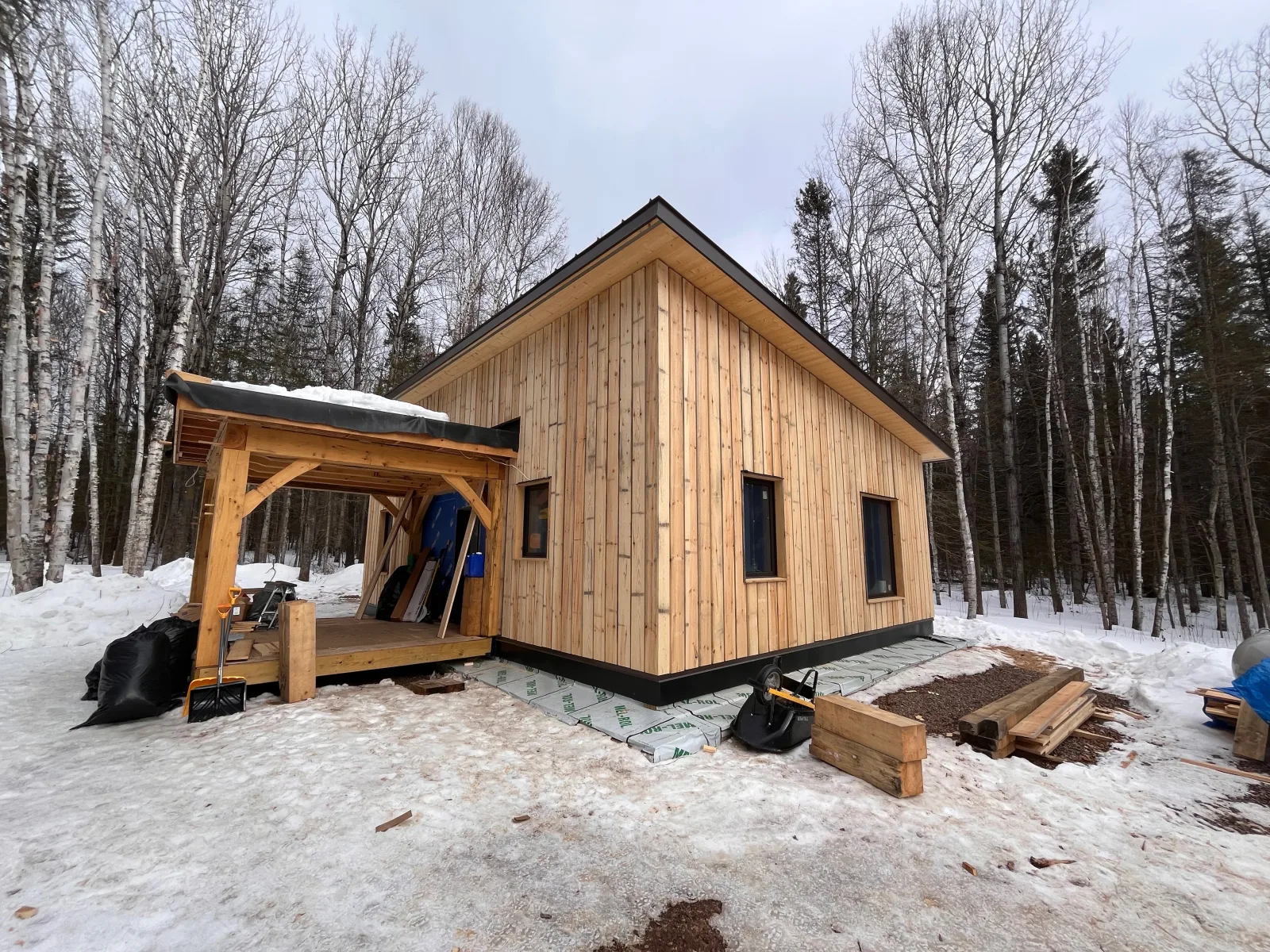 House 1 built at School House Road — cedar siding and timber-frame porch in a North Shore forest